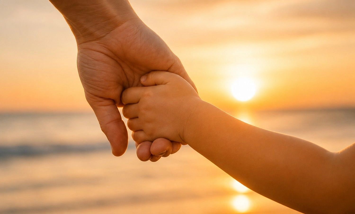 Michael | Child Heart Healing® - Gesundheits und Hypnose Coach - Eine Erwachsenenhand hält sanft die Hand eines Kindes vor einem warmen Sonnenuntergang am Meer.